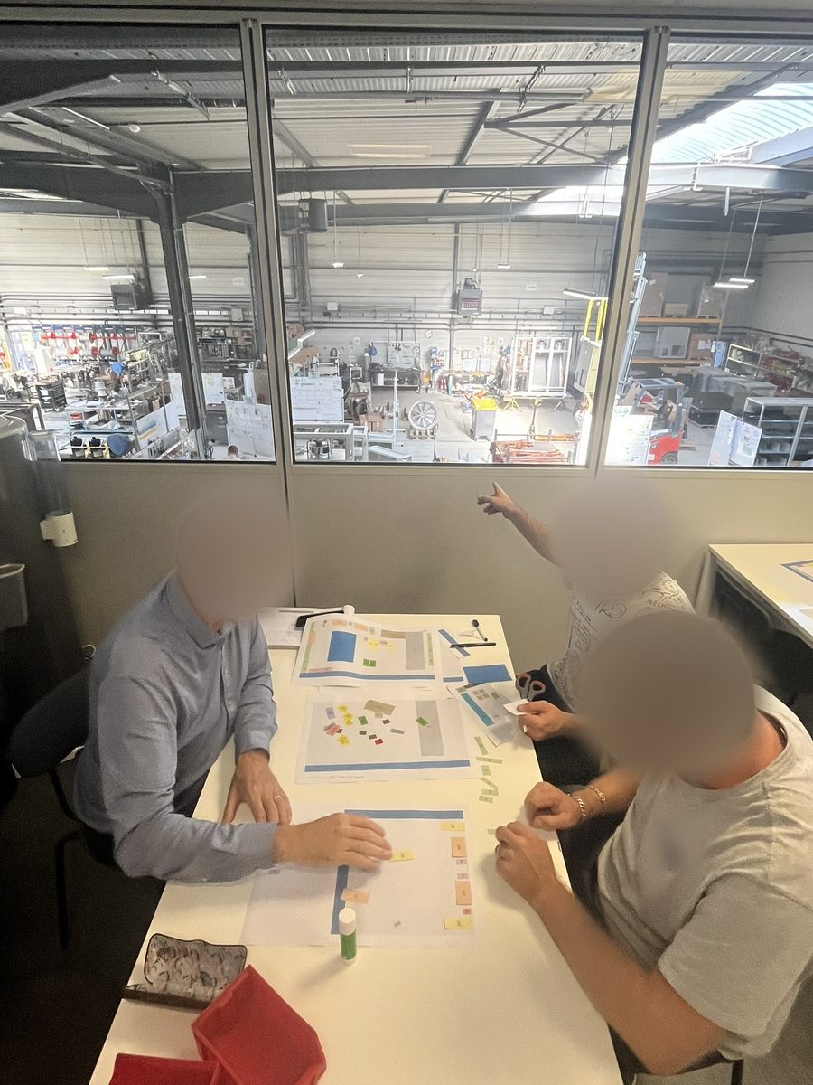 Trois personnes déplaçant des gabarits en papier sur des plans à l'échelle