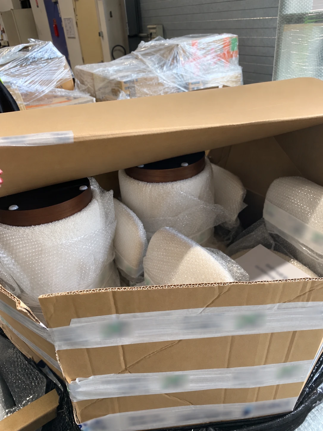 Carton en cours de fermeture en entrepôt, contenant plusieurs produits enveloppés individuellement dans du papier bulle.
